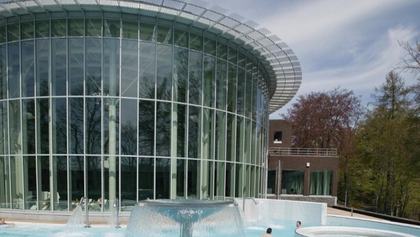A modern building with a glass facade and a pool area with a water feature.