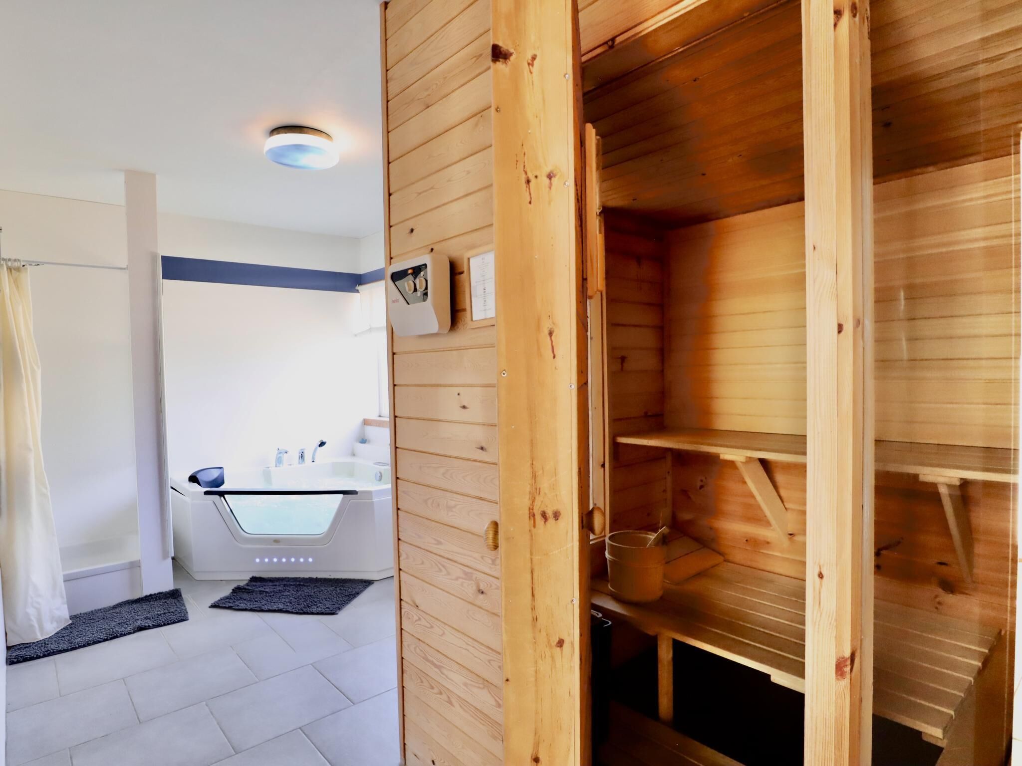 A modern bathroom with a glass-enclosed shower, a wooden sauna, and a white sink.