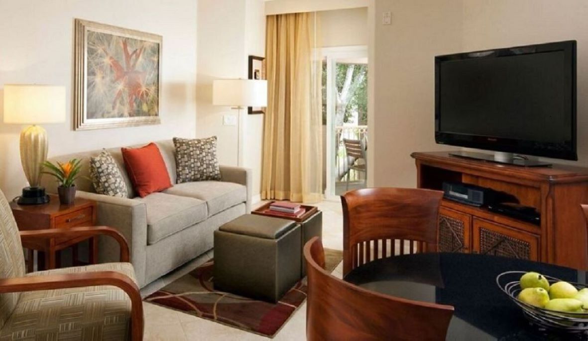 Una sala de estar con sofá, reposapiés, mesa de centro, televisor y un comedor con sillas y mesa.