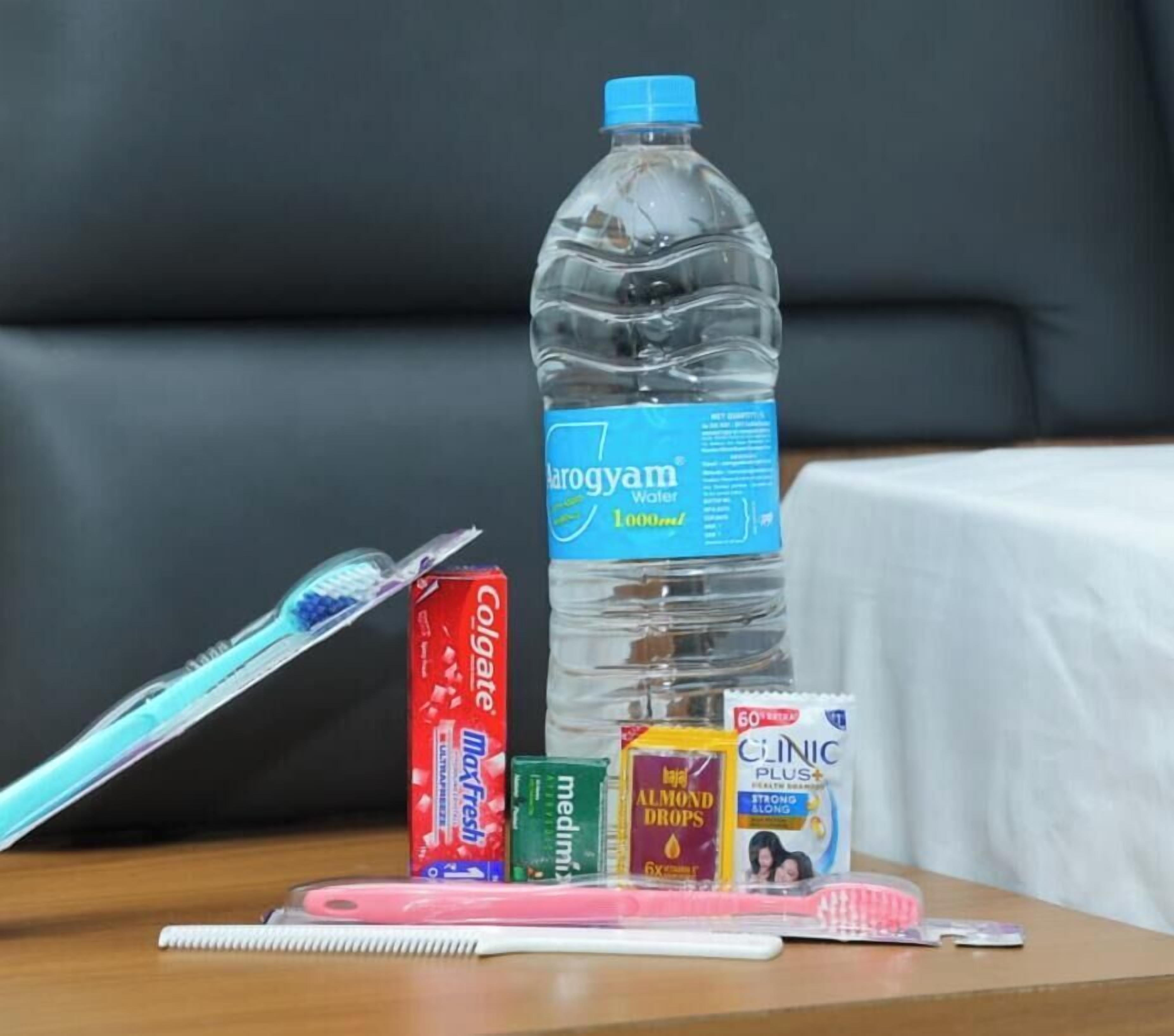 Una botella de agua, un cepillo de dientes, un tubo de pasta de dientes, un tubo de enjuague bucal, una caja de hilo dental y un peine sobre una mesa.