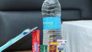 Una botella de agua, un cepillo de dientes, un tubo de pasta de dientes, un tubo de enjuague bucal, una caja de hilo dental y un peine sobre una mesa.