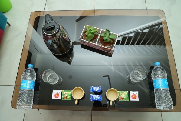 A glass-top table with a kettle, two potted plants, two water bottles, two cups, and two packets of tea. - SP24 Restaurant and Lodge (Jath)