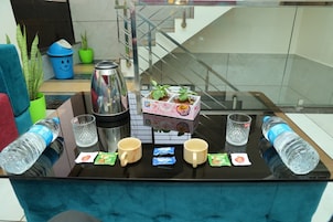 Zona de recepción de hotel con una mesa de centro de vidrio, botellas de agua, vasos y una pequeña exhibición de plantas.