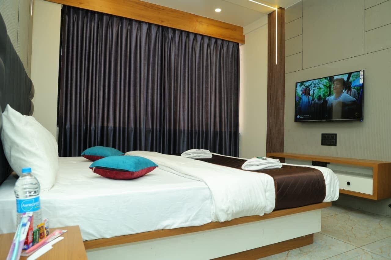 A modern hotel room with a large bed, a television, and a wooden bench.