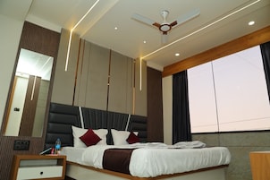 Una habitación de hotel moderna con una cama grande, un ventilador de techo, una mesita de noche y un ventanal amplio.