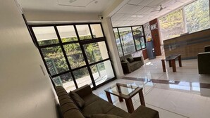 Un vestíbulo amplio con ventanas grandes, un sofá, una mesa de vidrio y una recepción.