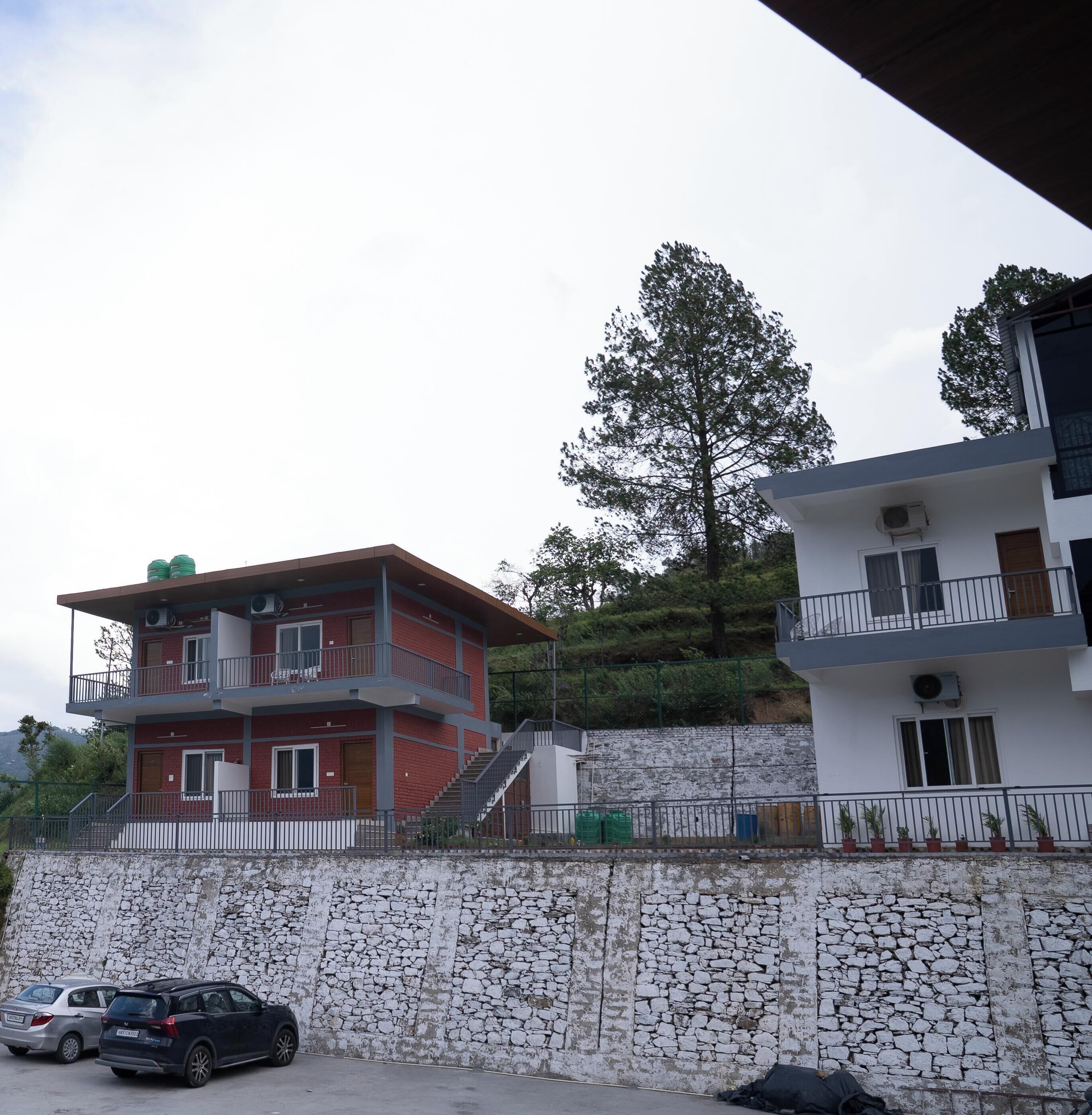A multi-story building with balconies, a stone wall, and parked cars.