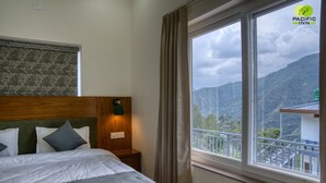 Un dormitorio con una cama grande, cabecera de madera, una mesita de noche, una lámpara de pared y una ventana con vistas a las montañas.