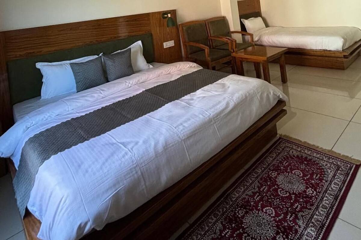 A hotel room with a large bed, a smaller bed, two chairs, a desk, and a ceiling fan.