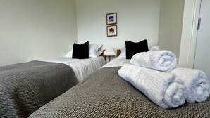 Une chambre d’hôtel avec deux lits simples, une table de chevet avec une lampe et une porte.