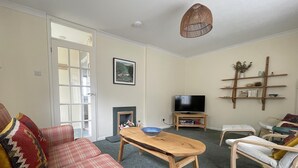 Un salon avec un canapé à carreaux, une table basse en bois, un téléviseur posé sur un meuble, une cheminée et une bibliothèque.
