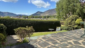 A landscaped garden with a stone patio, a neatly trimmed hedge, and a view of a town and mountains in the background. - 16 Manesty View -  a bungalow that sleeps 4 guests  in 2 bedrooms (Central Keswick)