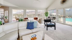 Un salon spacieux avec un canapé blanc, un ventilateur de plafond et de grandes fenêtres offrant une vue sur les montagnes.