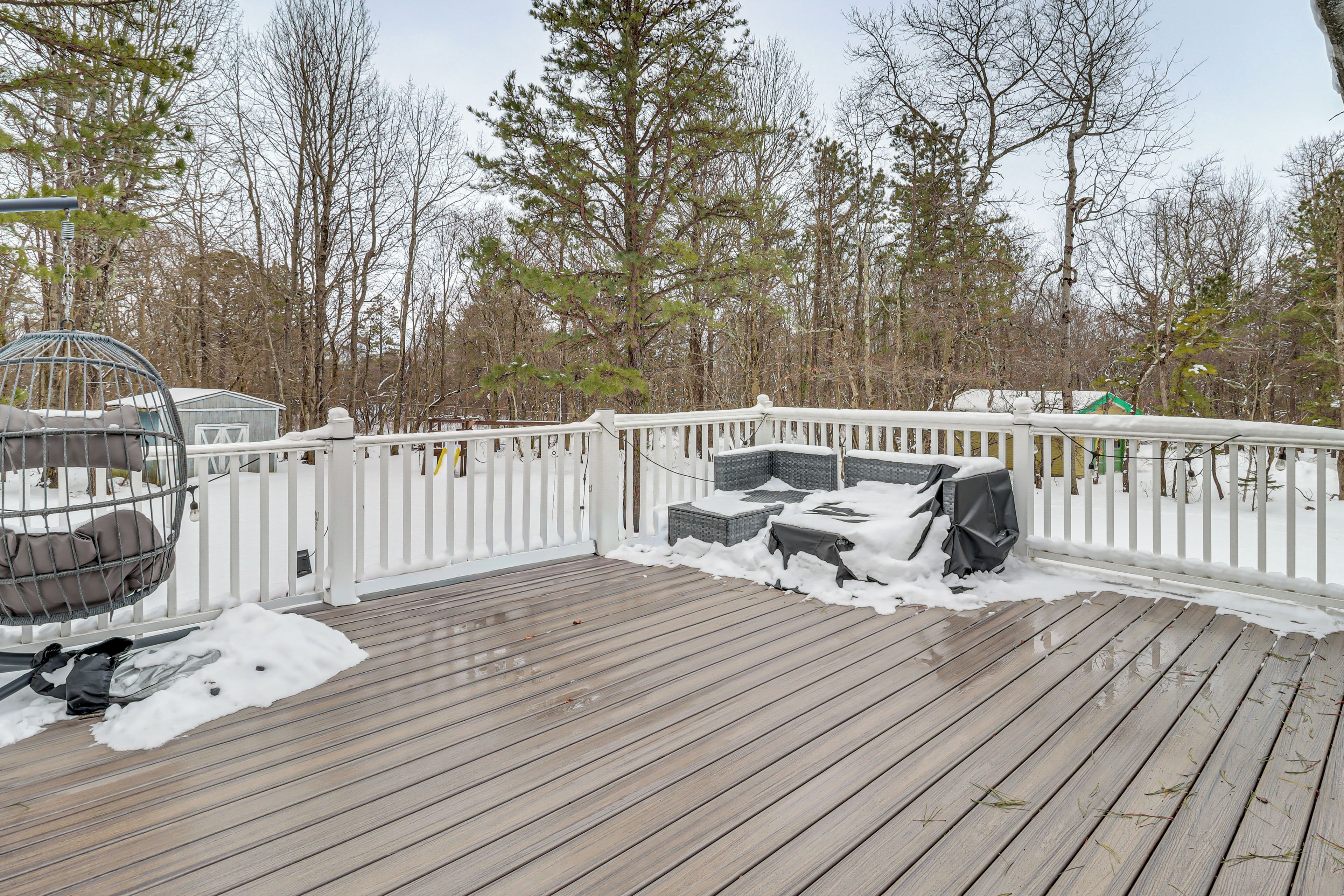 A wooden deck with a white railing, a covered seating area, and a bird feeder.