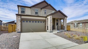 A two-story house with a garage, stone pillars, and a gravel driveway.