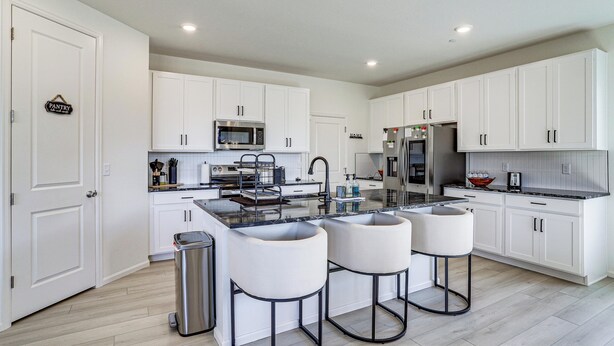 A modern kitchen with white cabinetry, a central island with bar stools, stainless steel appliances, and a trash can.