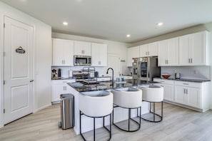A modern kitchen with white cabinetry, a central island with bar stools, stainless steel appliances, and a trash can. - WFH-Friendly Commerce City Home Near DIA (Commerce City)