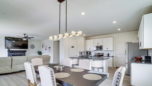 A modern kitchen with white cabinets, a central island, and a dining area with a dark wood table and white chairs.