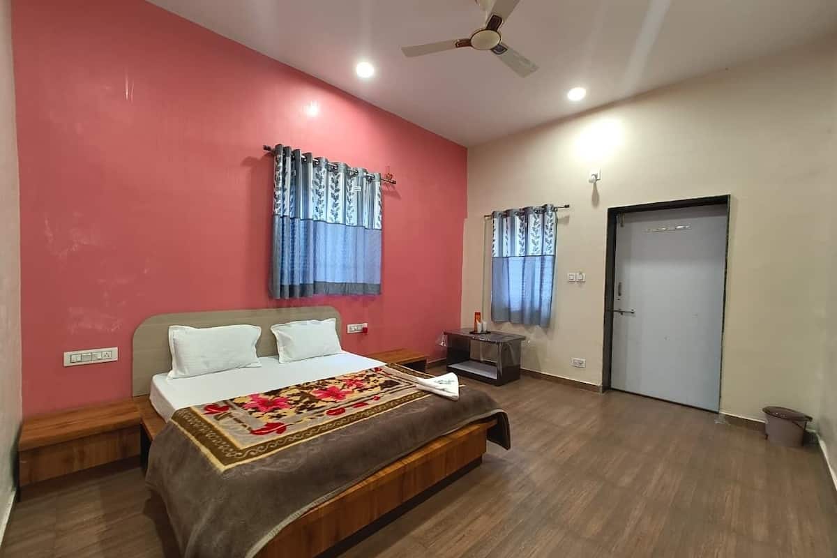 Quarto com cama, mesa de cabeceira, ventoinha no teto e uma porta.