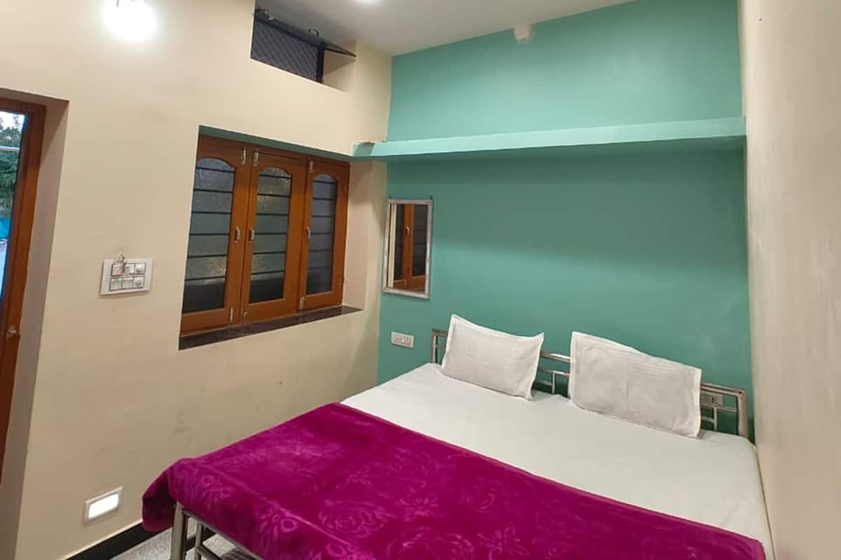 Quarto com cama, ventilador de teto, janela com molduras de madeira e interruptor de luz fixado na parede.