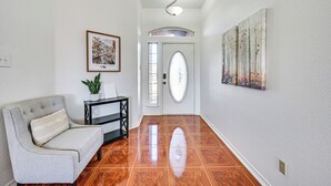Un pasillo con un sofá, una mesita con una planta, una puerta con un panel de vidrio decorativo y un cuadro colgado en la pared.