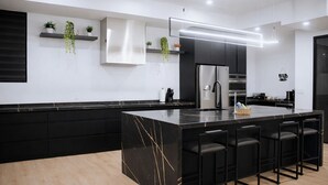 A modern kitchen with a large island, black cabinetry, and stainless steel appliances. - Grand, Spacious Villa in the Heart of Downtown High River (High River)