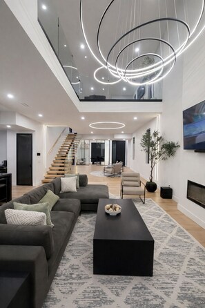 A modern living room with a staircase, a black coffee table, and a large TV. - Grand, Spacious Villa in the Heart of Downtown High River (High River)