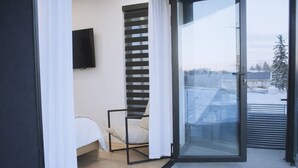 A bedroom with a bed, a chair, a TV, and a sliding glass door leading to a balcony. - Grand, Spacious Villa in the Heart of Downtown High River (High River)