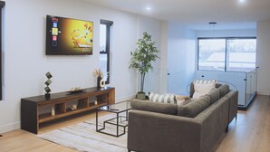 A modern living room with a sofa, coffee table, TV, and a plant. - Grand, Spacious Villa in the Heart of Downtown High River (High River)