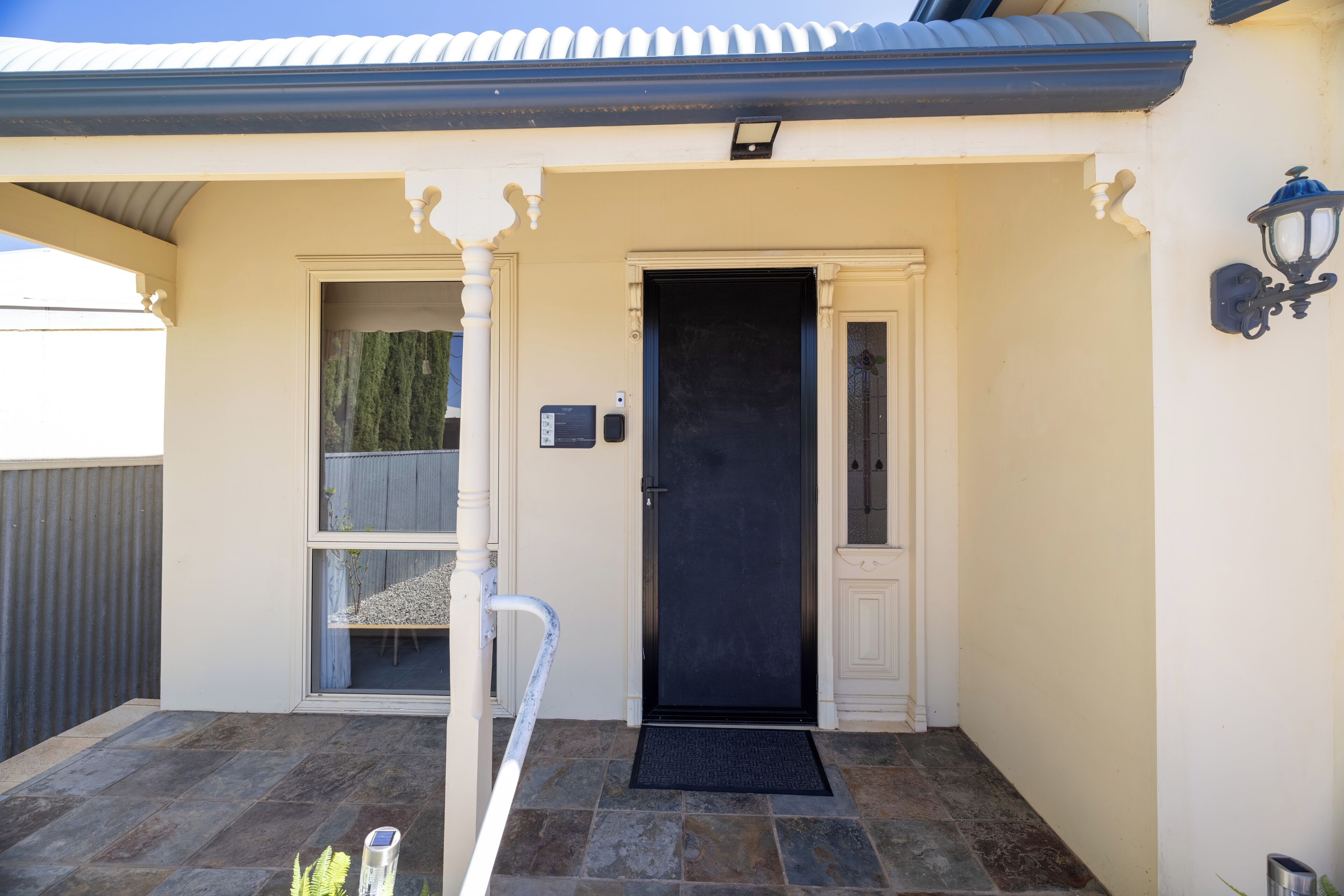 Une entrée de maison avec une porte noire, une petite fenêtre et un portail en métal.