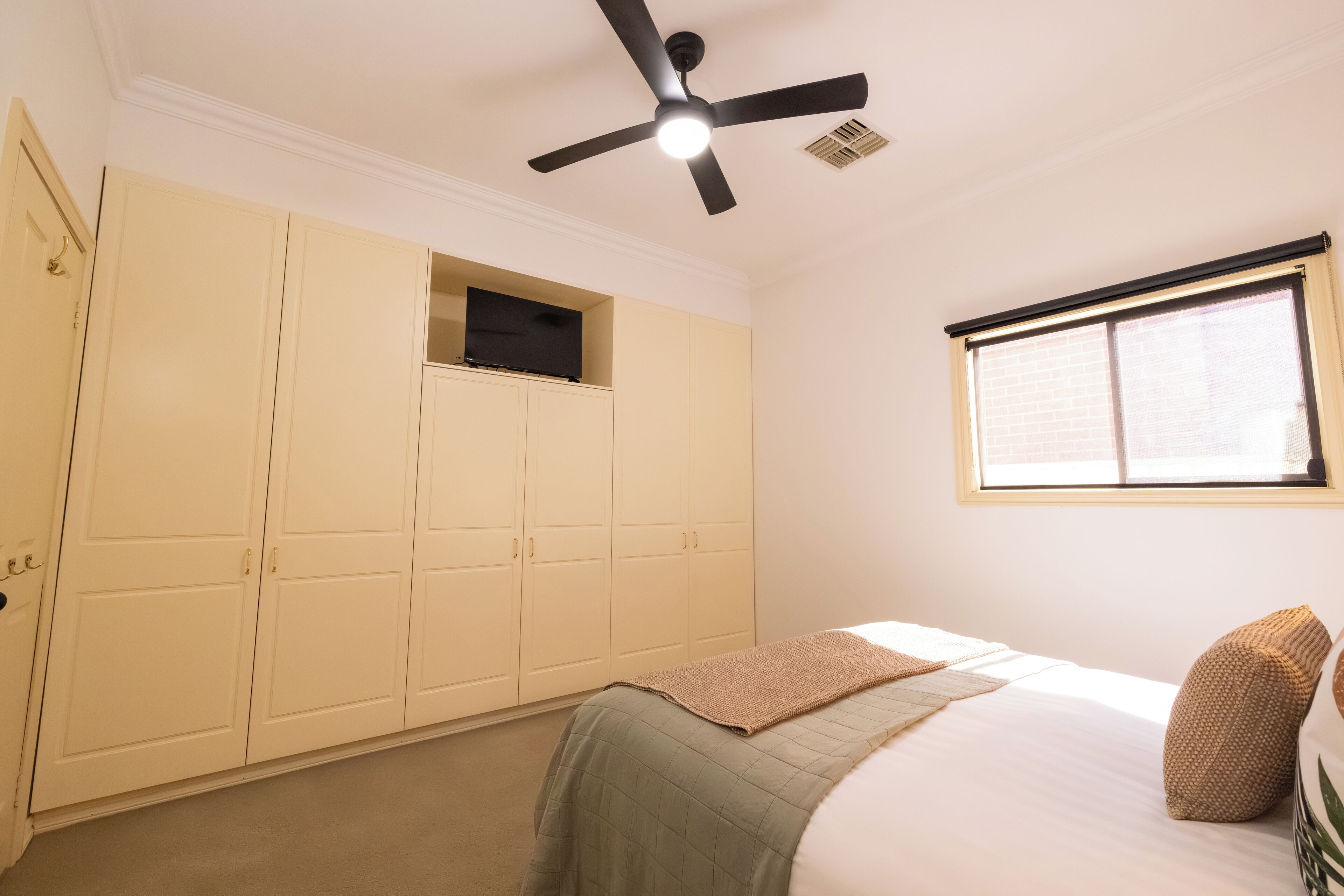 A bedroom with a bed, a ceiling fan, a window, and a wardrobe.