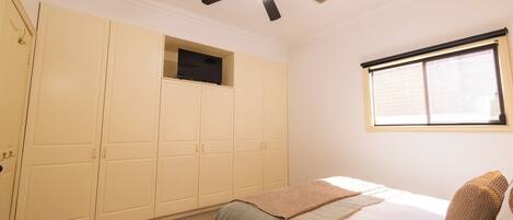 Un dormitorio con cama, ventilador de techo, ventana y armario.