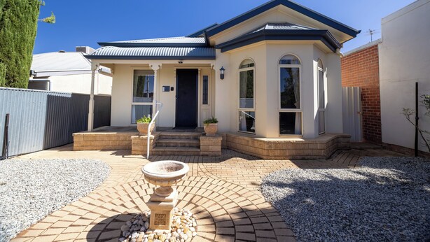 Una casa a due piani con un portico, una fontana in pietra e un vialetto in mattoni che conduce all'ingresso.