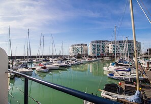 A marina with multiple boats docked, a building with balconies in the background, and a clear sky.
