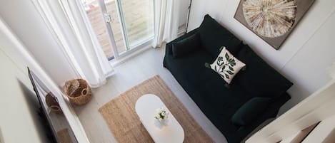 A modern living room with a dark green sofa, a white coffee table, and a large window with blinds.