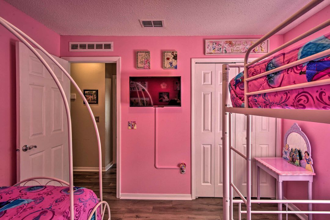 Un dormitorio con decoración rosa, con literas, una puerta y un estante pequeño con fotografías.
