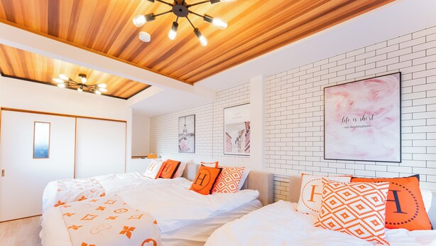 A hotel room with a wooden ceiling, white brick walls, and a bed with orange and white bedding. - Recommended for USJ, Osaka Sight Seeing,Newly Reno! 5min walk to station. 2bed (Osaka)