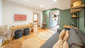 Ein modernes Wohnzimmer mit einer Couch, einem Holztisch, einem Fernseher und einer Küche im Hintergrund.