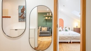 Ein modernes Schlafzimmer mit Bett, Nachttisch und Schreibtischchen. An der Wand hängt ein Spiegel, und eine Tür führt in einen weiteren Raum.