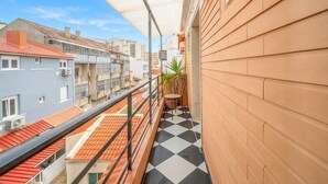 Ein Balkon mit kariertem Boden, einem Blumentopf und Blick auf angrenzende Gebäude.
