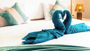 Een net opgemaakt bed met een handdoek in de vorm van een hart, een decoratieve wandhanger en een bedlampje.