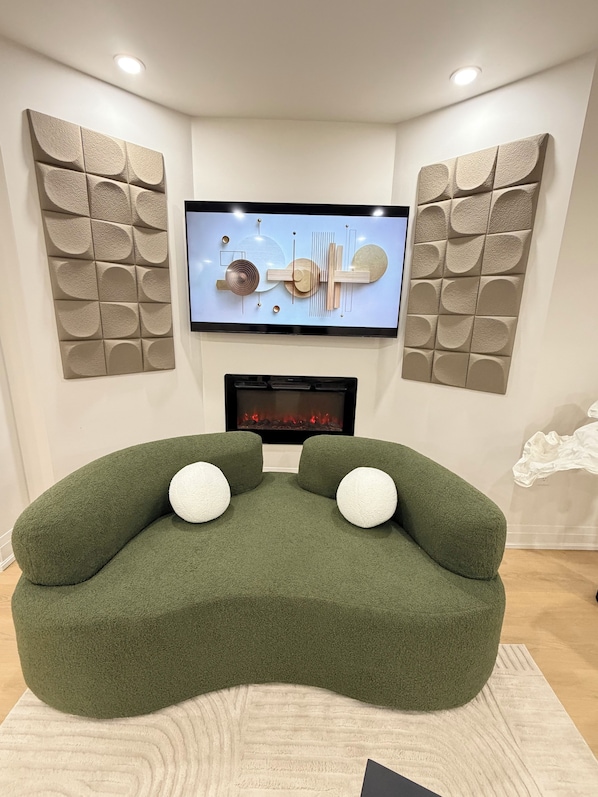 Een moderne woonkamer met een groene bank, een flatscreen televisie, decoratieve wandpanelen en een open haard.