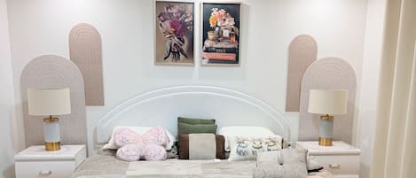 A bedroom with a large bed, two bedside tables, a headboard, and two wall-mounted lamps.