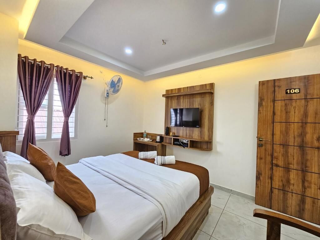 A hotel room with a bed, a TV mounted on a wooden panel, a wardrobe, and a window with curtains.