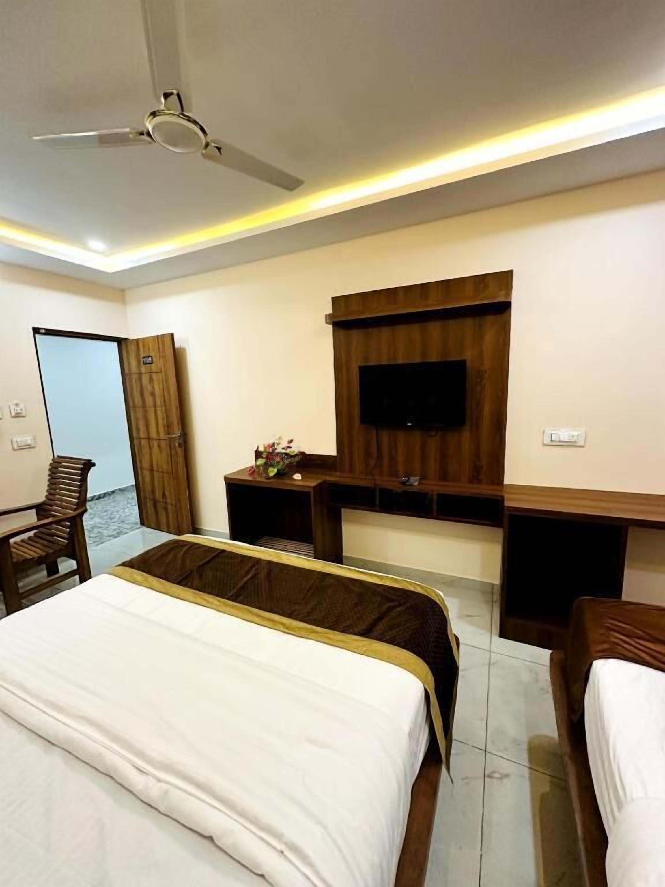 Una habitación de hotel con cama, escritorio, silla, televisor montado en la pared y ventilador de techo.