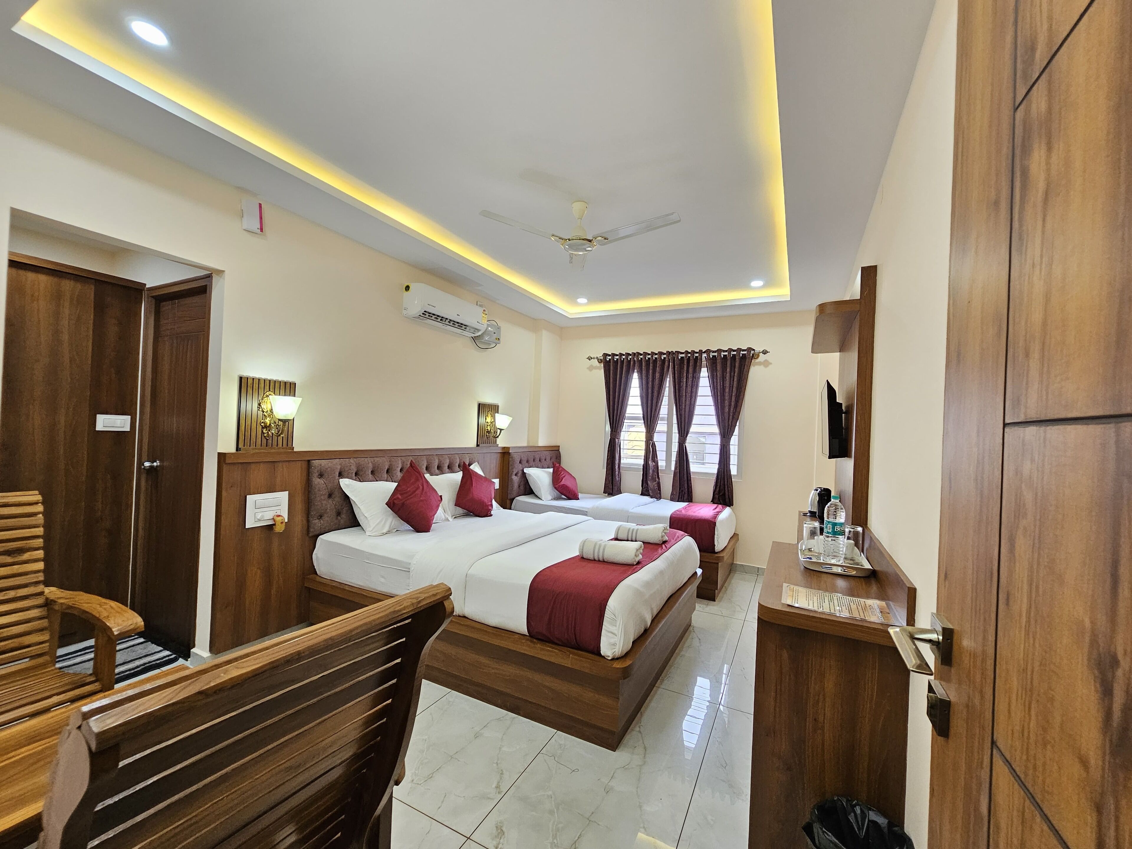 A hotel room with two beds, a desk, a chair, a ceiling fan, and an air conditioning unit.