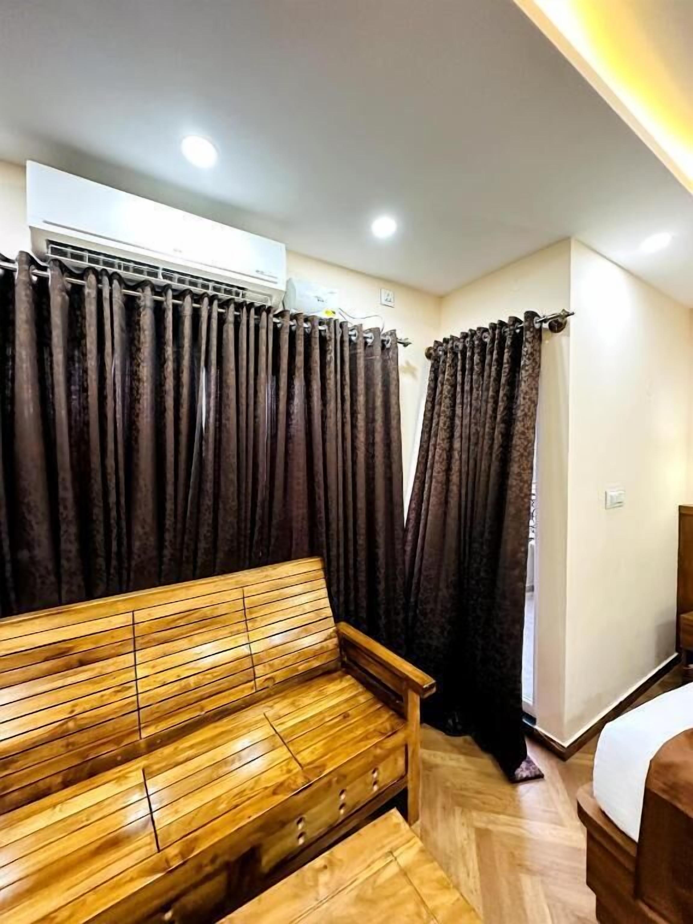 A room with a wooden bench, dark curtains, an air conditioning unit, and a bed.