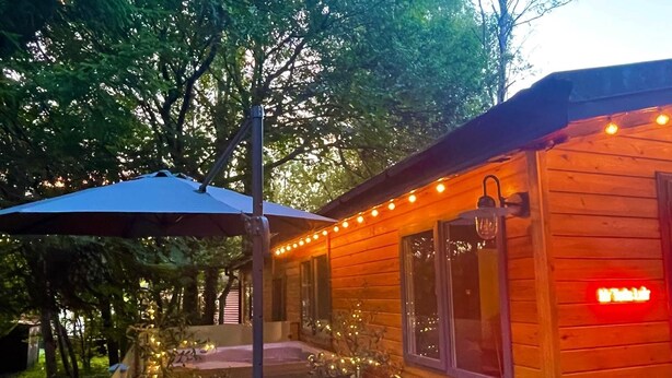 Una cabaña de madera con un porche, escalones e iluminacion de luces colgantes.