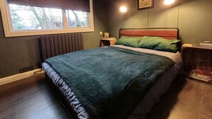 Un dormitorio con cama, ventana, radiador, mesita de noche y lámpara de pared.