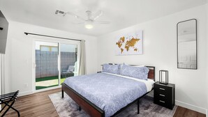 Ein Schlafzimmer mit Bett, Nachttisch, einer Weltkarte an der Wand, einer Glasschiebetür zu einem Balkon und einem Deckenventilator.
